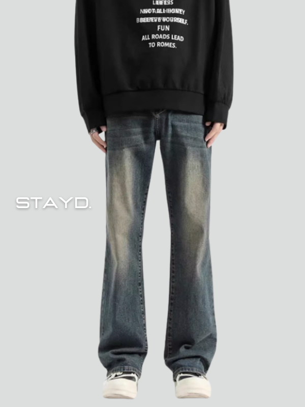STAYDのロゴが入った背景でデニムを穿いた男性が正面を向いて立っている。韓国系メンズカジュアルコーデに最適。